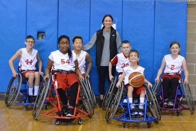 Young wheelchair basketball team in white jerseys poses with a coach