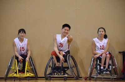 Three players in white jerseys 15, 35 and 12 sit side by side in a gym