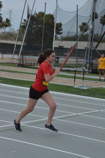 Young athlete in a red T-shirt runs along the track by the throwing cage