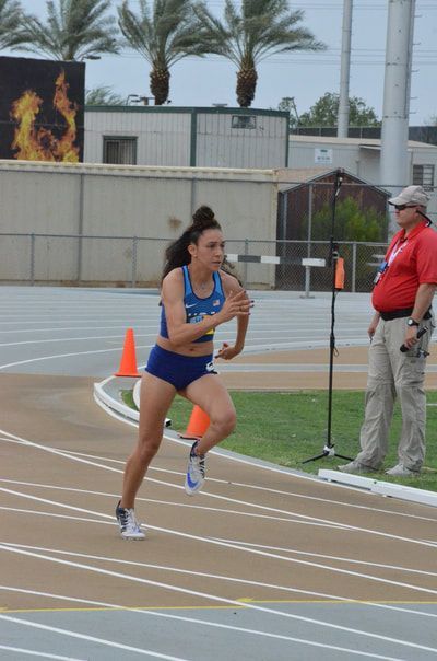 Sprinter in a blue uniform comes off the curve past an official