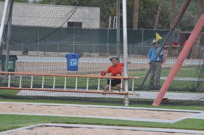 Athlete in red sits in the throwing cage as an official holds a flag