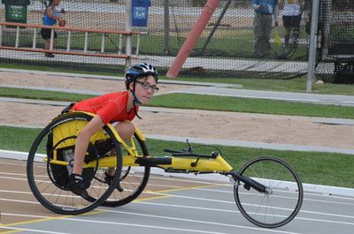 Young racer in a red top pushes a yellow racing wheelchair