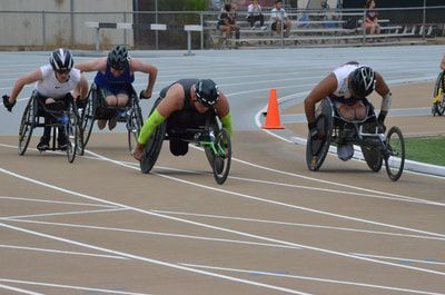 Four wheelchair racers come off the curve, one in green arm sleeves
