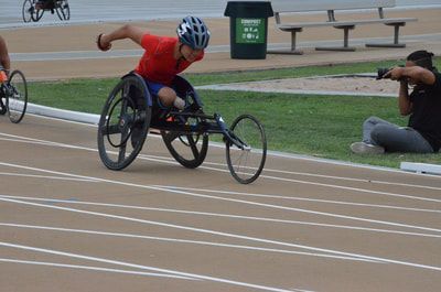 Racer in a red top leans into a push as a photographer kneels nearby