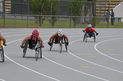 Racers in red and white helmets push side by side down a gray track