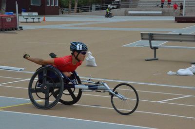 Racer in a red top swings arms back mid-push in a black racing chair