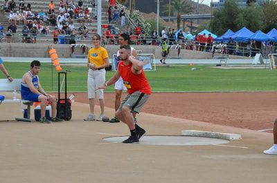 Shot putter in an orange tank top gets set in the circle before a crowd