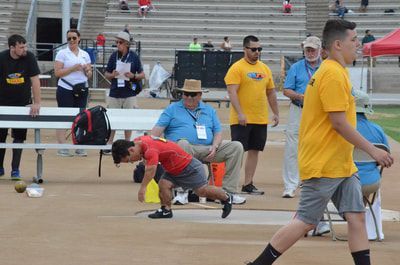 Young athlete in red bends low in the shot put circle among officials