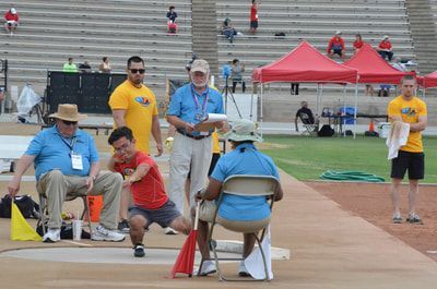 Young athlete in red releases a throw as seated officials watch