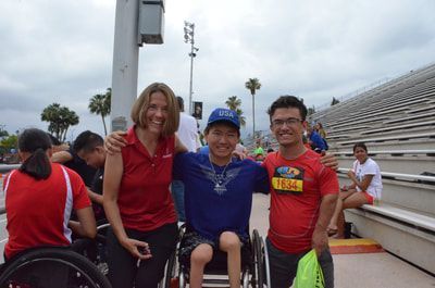 Coach in a red polo poses with athletes, one in a USA cap, by the stands