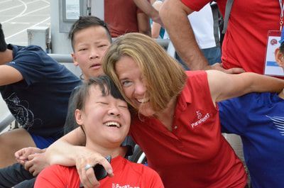 Coach in a red ParaSport polo hugs a laughing athlete