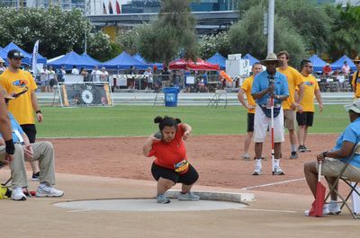 Young athlete in an orange top crouches in the shot put circle