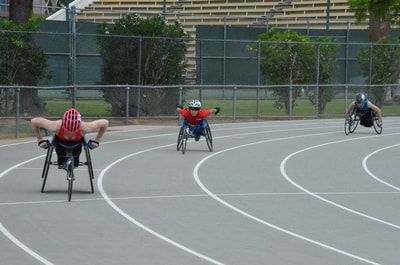 Three wheelchair racers spread out across the bend of a gray track
