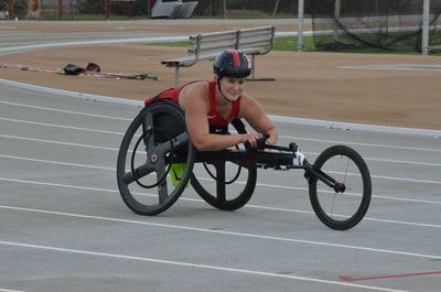 Smiling wheelchair racer in a red top rounds the bend in a black chair
