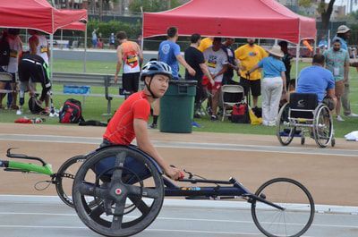 Young wheelchair racer in a red shirt passes the team tents