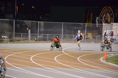 Two wheelchair racers and a runner round the curve during an evening race