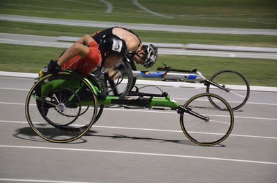 Two wheelchair racers, one in a green chair, battle side by side