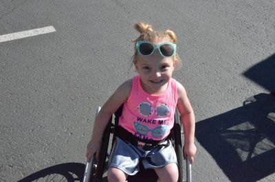 Smiling young girl in a pink tank top and sunglasses in her wheelchair