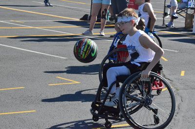 Young player in a white tank top and bandana dribbles the ball up the court