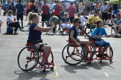 Player in navy carries the ball as two others follow in red wheelchairs