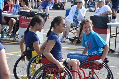 Three smiling girls in wheelchairs, two in navy and one in light blue