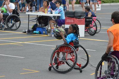Young girl in a light blue shirt dribbles the ball in a red wheelchair