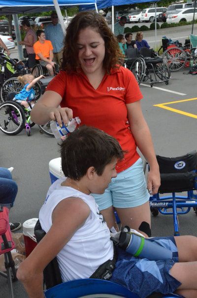 Woman in a red ParaSport shirt pours water to cool off a young player
