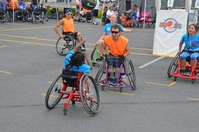 Kids in light blue and players in orange shirts roll across the court