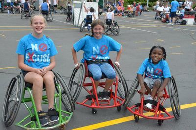 Three smiling girls in blue No Excuses shirts pose in their wheelchairs