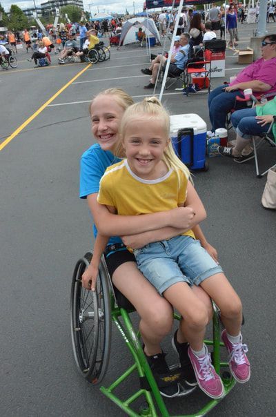 Young girl in yellow sits on a smiling player's lap in a green wheelchair
