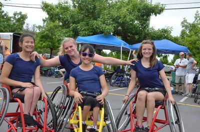 Four women in navy shirts pose close together in their sport wheelchairs