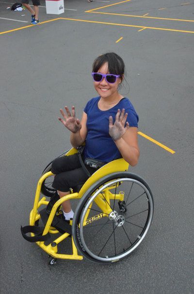Player in purple sunglasses waves both hands from a yellow wheelchair