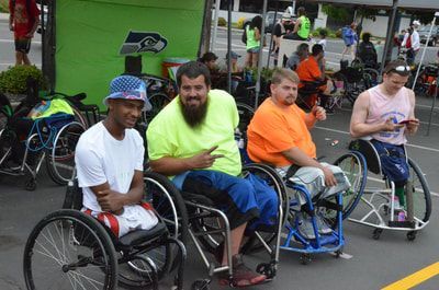 Four men in wheelchairs wait along the sideline, one pointing at the camera
