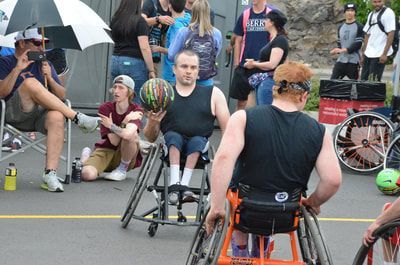 Player in a black tank top holds the ball as a fan under an umbrella films