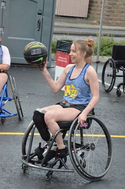 Smiling player in a blue tank holds the ball up in one hand on a wet court