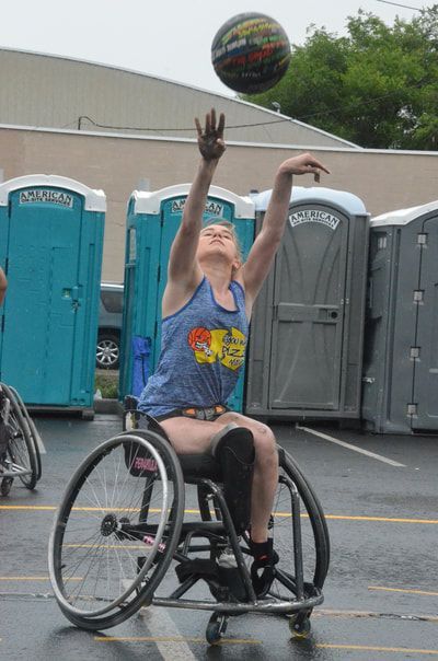 Player in a blue tank shoots at Hoopfest, the ball in the air above her arms