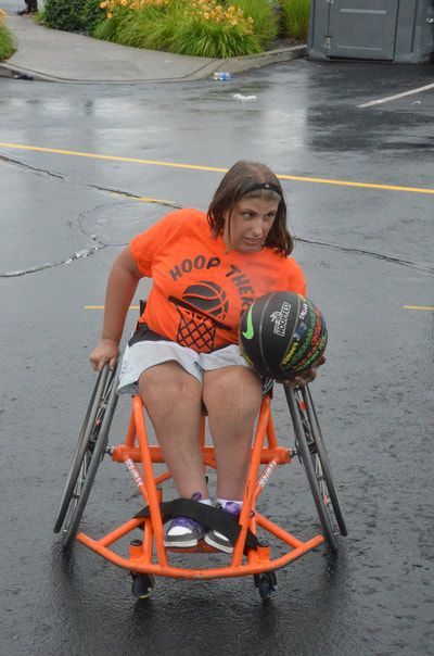 Player in an orange shirt rides her orange wheelchair with the ball in her lap