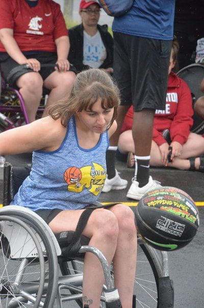 Player in a blue tank leans down to dribble the ball beside her wheel