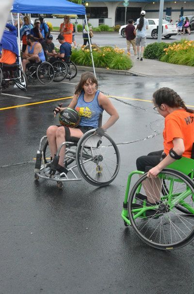 Player in a blue tank with the ball faces a defender in a green wheelchair