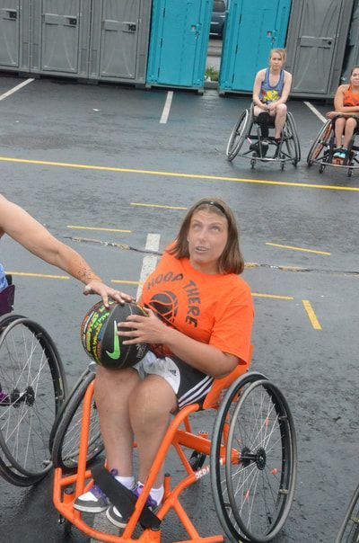 Player in an orange wheelchair holds the ball as a hand reaches in to defend