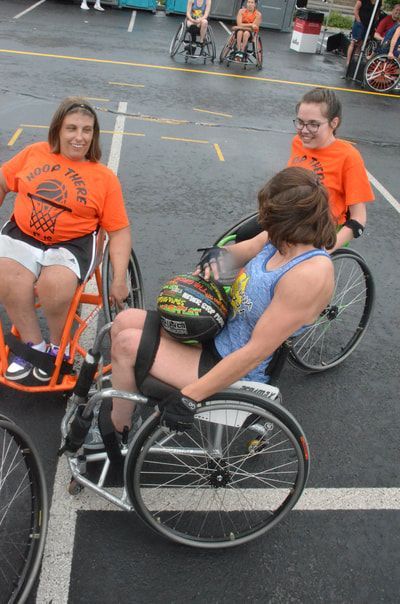 Player in a blue tank holds the ball in her lap between two players in orange