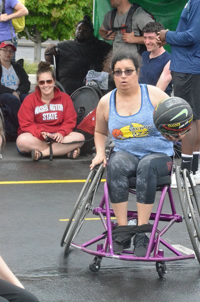 Player in sunglasses and a blue tank carries the ball past seated spectators
