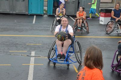 Player in a blue wheelchair grips the ball at her chest as a defender waits