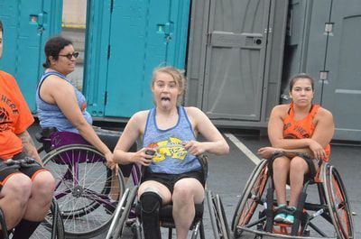 Player in a blue tank sticks out her tongue between a teammate and an opponent