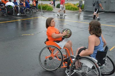 Player in orange passes the ball from her orange wheelchair as a defender turns