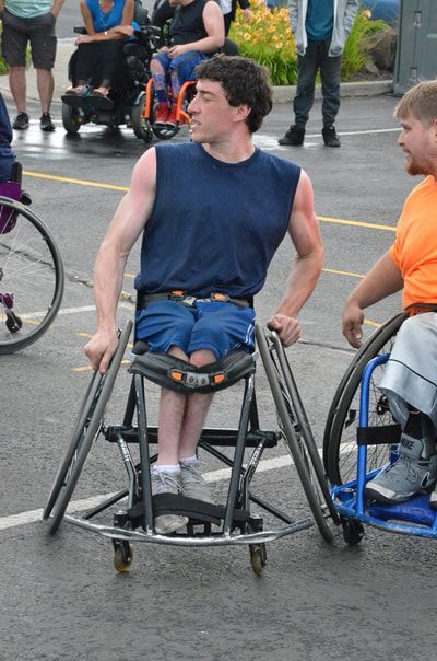 Young man in a navy tank pushes his wheelchair while glancing to the side