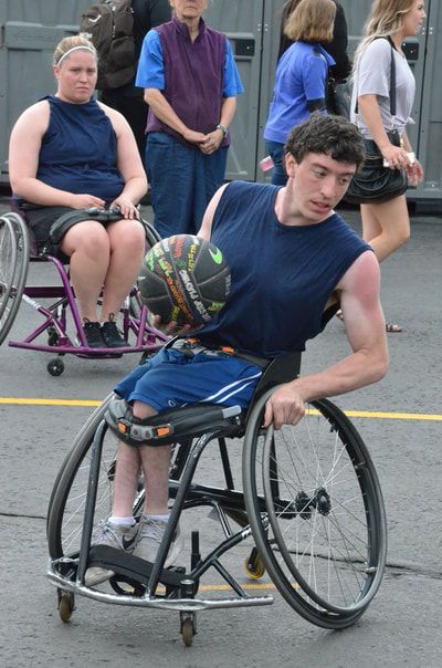 Player in a navy tank dribbles low past a seated player in a purple chair