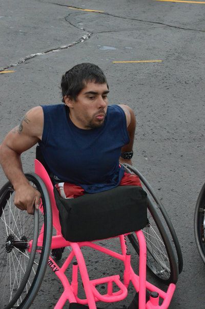 Player in a navy tank in a bright pink wheelchair watches the play