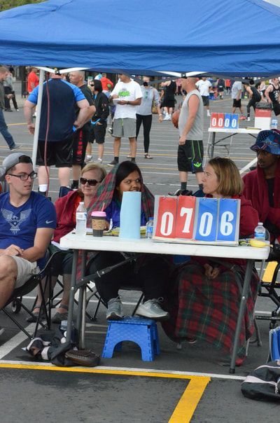 Hoopfest scorekeepers under a blue canopy beside a flip scoreboard showing 07 06