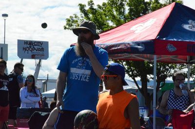 Bearded man in a blue Justice shirt watches the game, hand at his chin